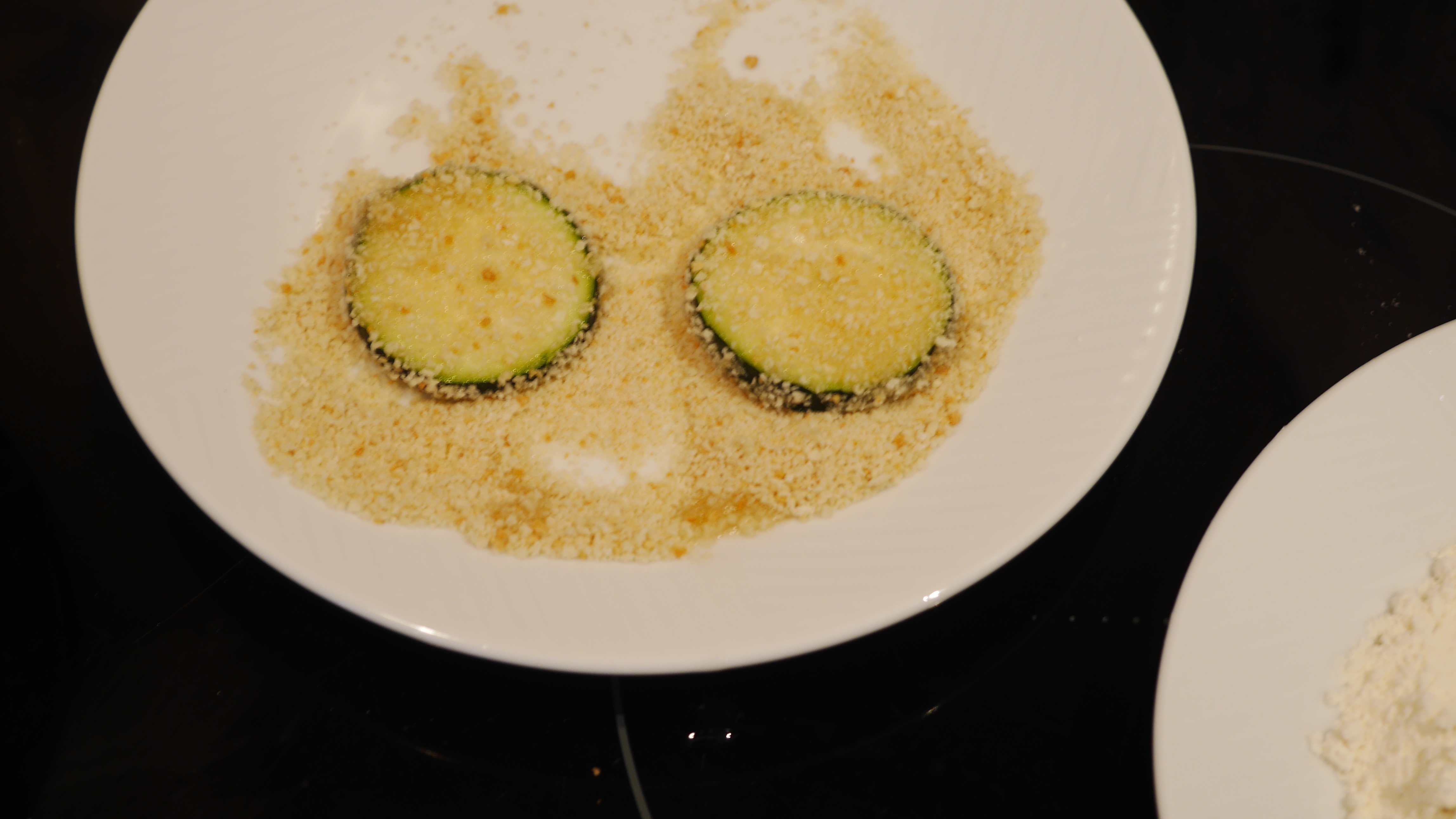 Two courgettes in breadcrumbs on a white plate