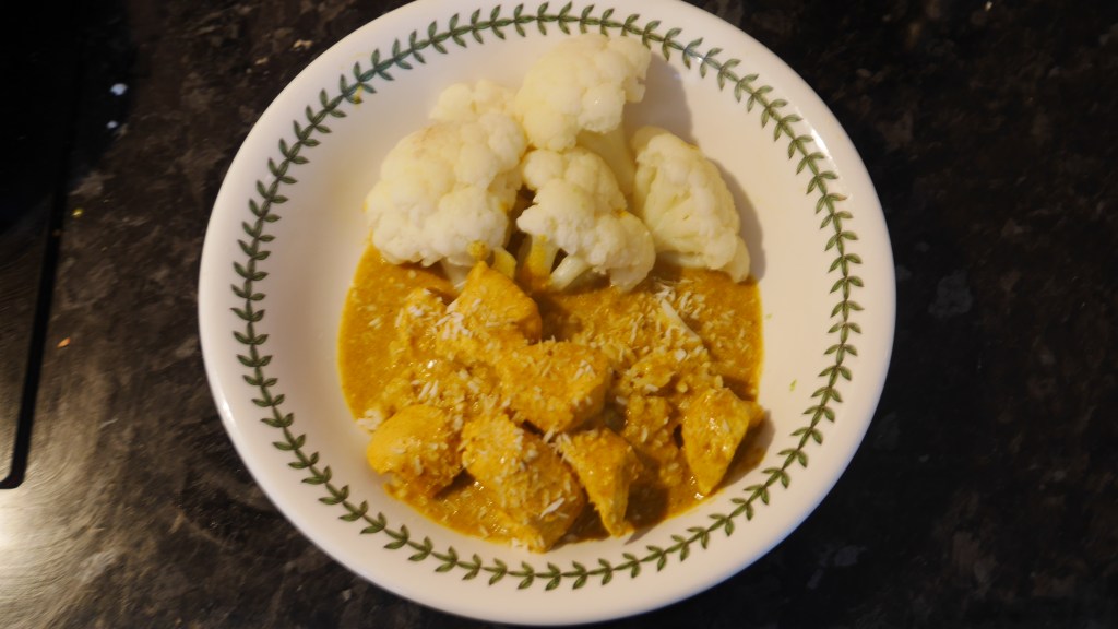 Bowl of chicken korma with dessicated coconut, and cauliflower.