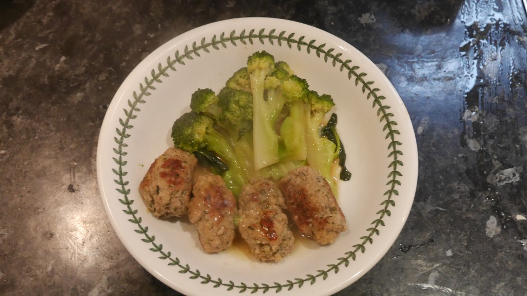 A bowl with four cooked sausages and broccoli in.