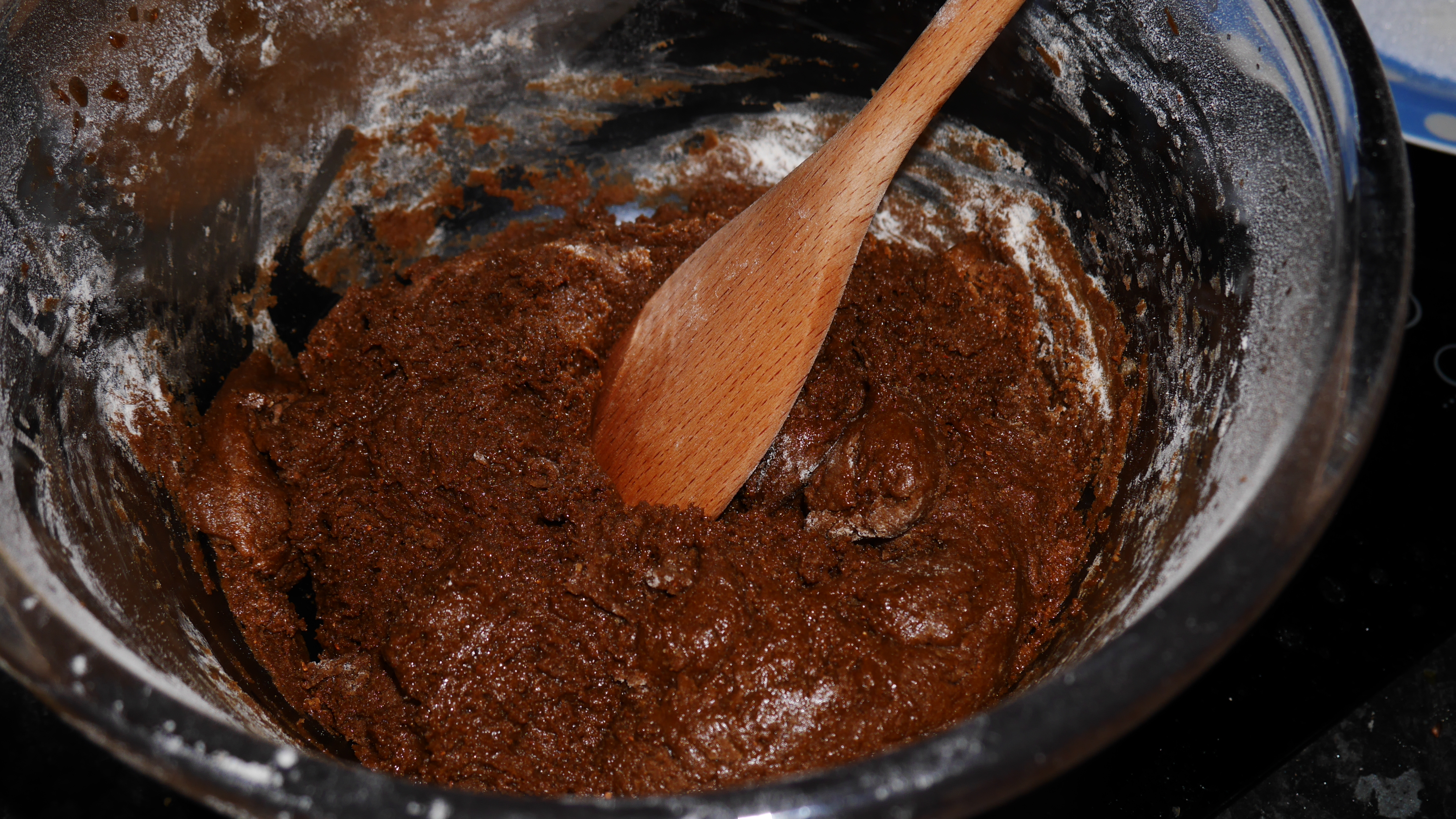 A clear mixing bowl with a brown mixture with a wooden spoon in it.