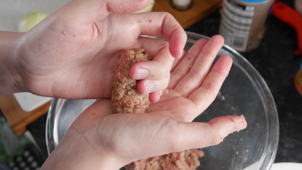 Alex squashes the end of the sausage into her right hand using her left.