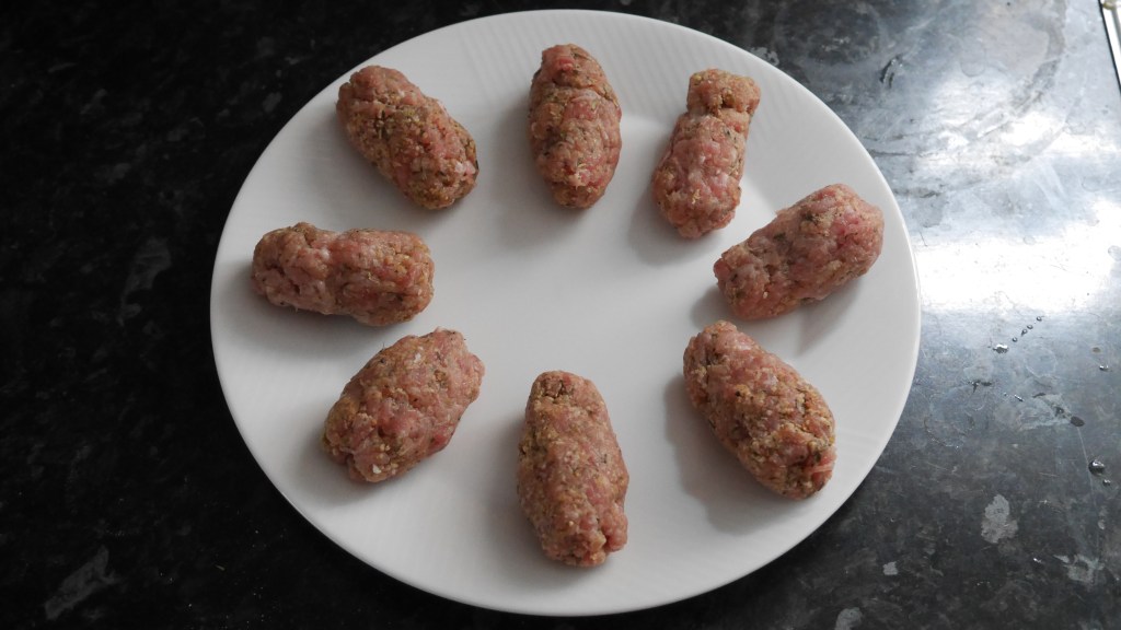 Eight uncooked sausages arranged in a circle on a white plate.